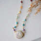 Freshwater pearl and rainbow chakra gemstone necklace. A white pearl, bezeled in gold or sterling silver sits at the center of the necklace below a handmade chain of rainbow stones. The gold style is shown.