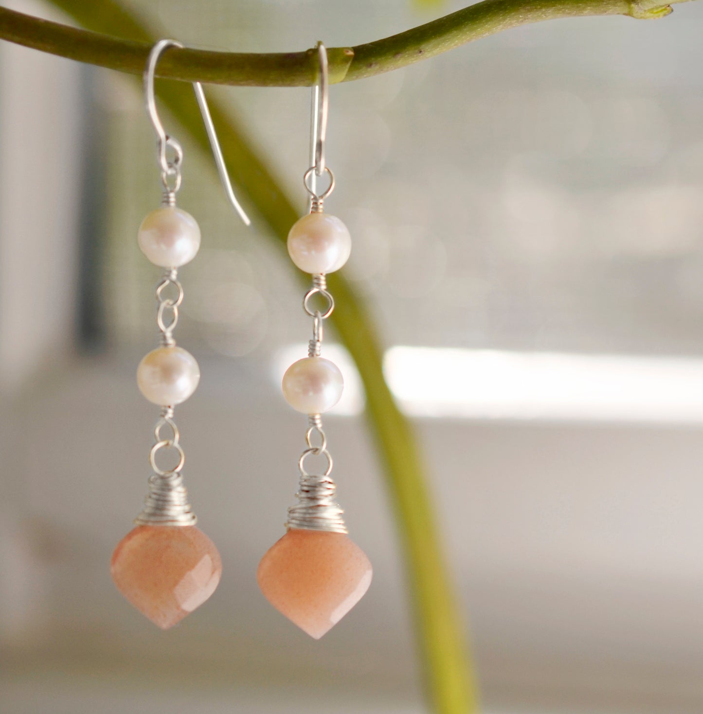 Two white semi-round pearls hang over natural peach Moonstone faceted drops. The silver style is shown.