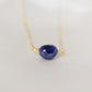 Small blue sapphire stone set onto a gold chain. The stone is a puffed oval shape. 