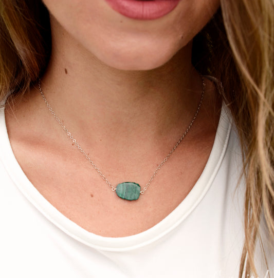 Natural green Malachite smooth polished slice with raw edges. Each stone is an irregular oval shape and has a variety of banding. Shown on a sterling silver chain. Modeled image.
